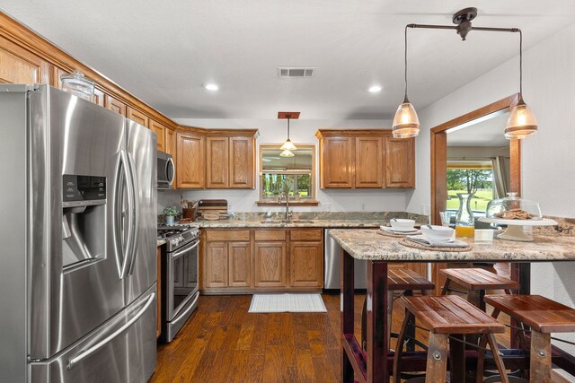 kitchen featuring appliances with stainless steel finishes, a sink, dark wood finished floors, brown cabinetry, and visible vents