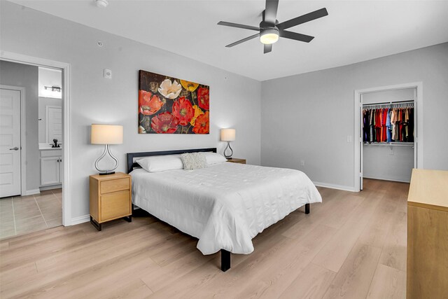 bedroom featuring a walk in closet, light wood finished floors, ensuite bath, baseboards, and a closet