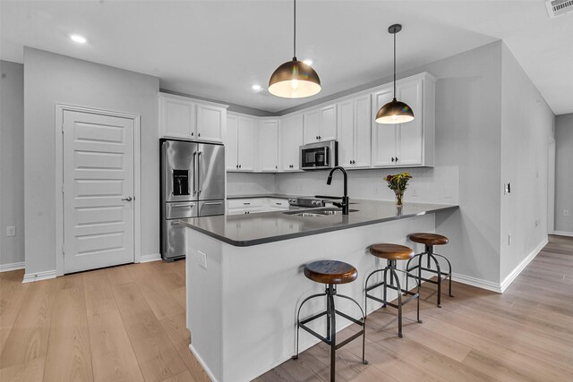 kitchen with a peninsula, appliances with stainless steel finishes, white cabinetry, and a sink