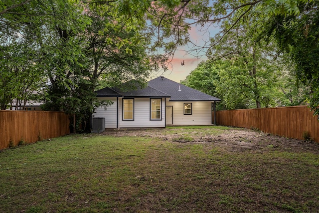518 S Cockrell Hill Rd, Cockrell Hill, TX 75211 - back of house at dusk with a yard, a fenced backyard, roof with shingles, and central air condition unit