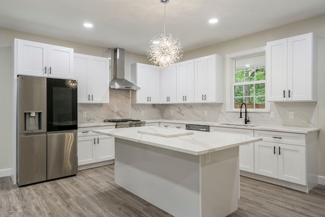 518 S Cockrell Hill Rd, Cockrell Hill, TX 75211 - kitchen featuring wall chimney range hood, appliances with stainless steel finishes, a center island, light wood finished floors, and an inviting chandelier