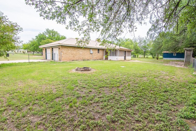 view of yard featuring a sunroom, an outdoor fire pit, and fence