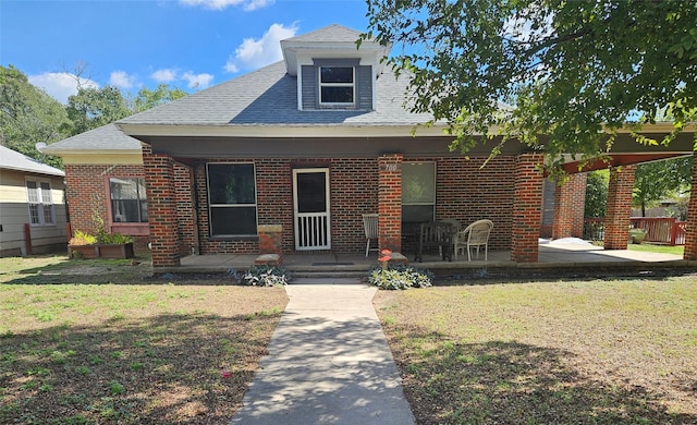 bungalow-style home featuring roof with shingles, a patio, a front yard, and brick siding