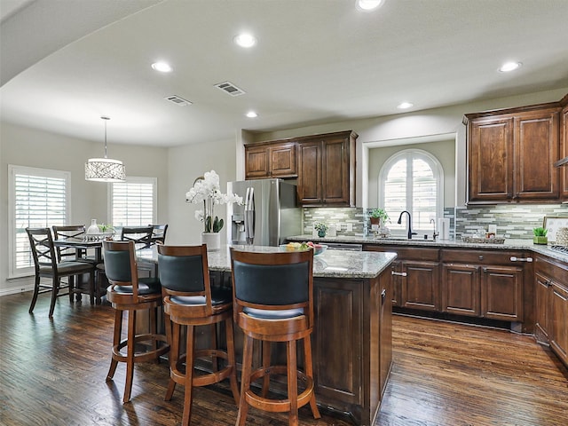 kitchen with a kitchen island, stainless steel refrigerator with ice dispenser, visible vents, and tasteful backsplash