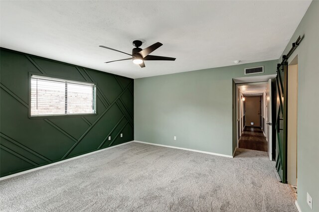 unfurnished bedroom with carpet flooring, a barn door, a decorative wall, baseboards, and visible vents