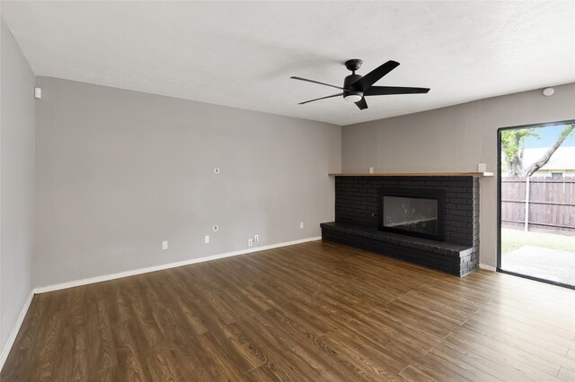 unfurnished living room with baseboards, a ceiling fan, a brick fireplace, and wood finished floors