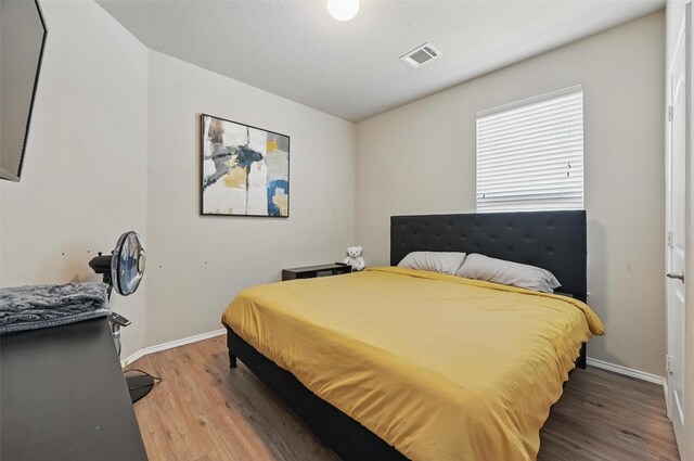 bedroom with baseboards, visible vents, and wood finished floors