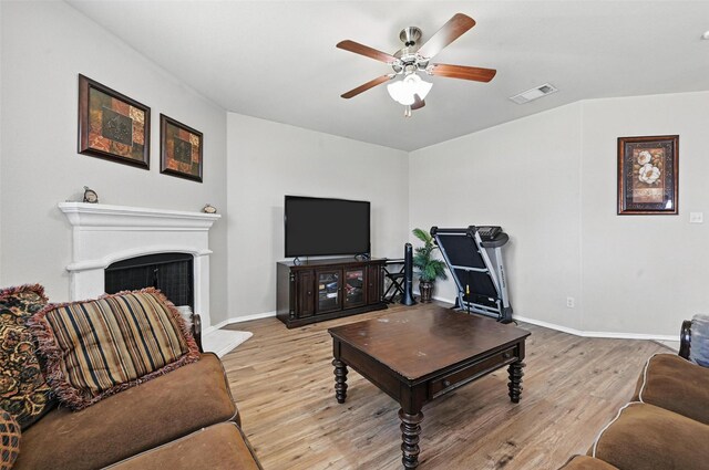 living area featuring visible vents, baseboards, ceiling fan, a fireplace with raised hearth, and light wood-style flooring