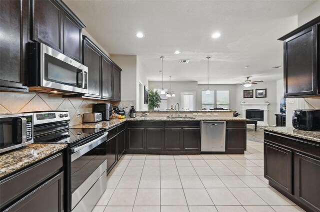 kitchen with a ceiling fan, appliances with stainless steel finishes, a sink, light stone counters, and a peninsula