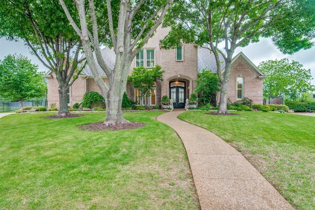 view of front of property with brick siding, fence, french doors, and a front yard