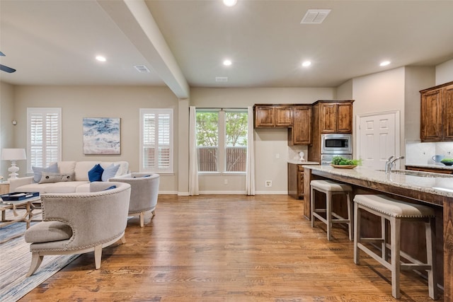 kitchen featuring a sink, a breakfast bar area, stainless steel microwave, light wood-type flooring, and visible vents