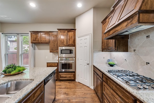 kitchen featuring light stone countertops, appliances with stainless steel finishes, custom range hood, light wood-type flooring, and visible vents