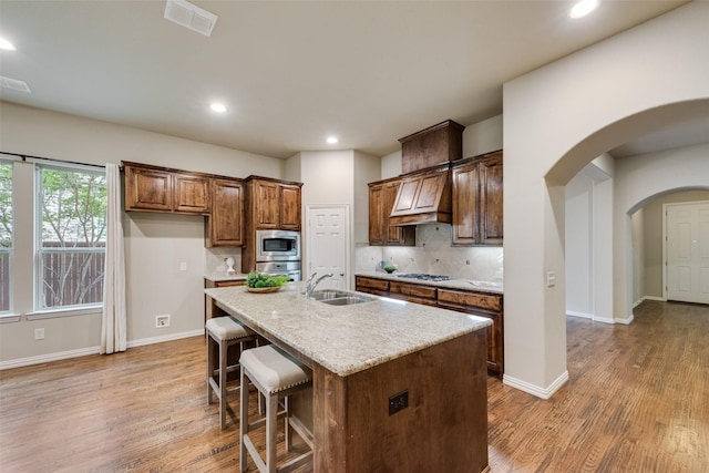 kitchen with a sink, stainless steel microwave, light wood finished floors, and visible vents