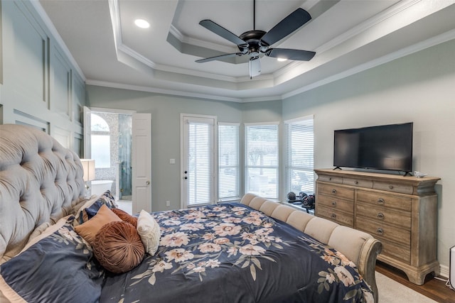 bedroom featuring ornamental molding, wood finished floors, a tray ceiling, and multiple windows