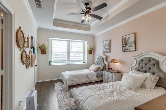 bedroom featuring baseboards, wood finished floors, a tray ceiling, visible vents, and ornamental molding