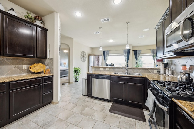 kitchen with dark brown cabinetry, appliances with stainless steel finishes, a sink, backsplash, and visible vents