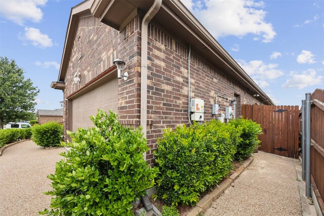 view of side of home featuring fence, a gate, a garage, and brick siding