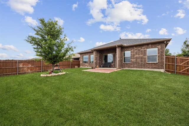 back of property with a yard, brick siding, a fenced backyard, and a patio area