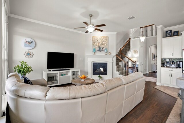 living area with crown molding, a glass covered fireplace, visible vents, dark wood-style floors, and stairway