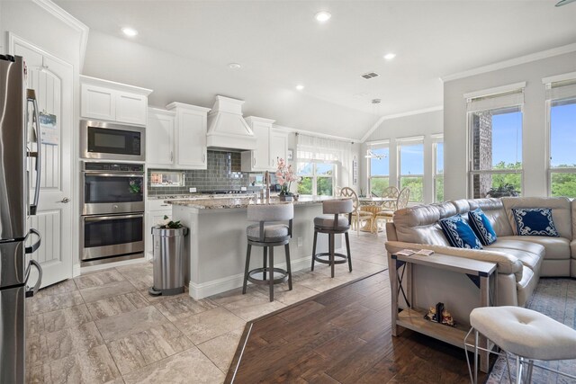 kitchen with visible vents, crown molding, appliances with stainless steel finishes, light stone countertops, and custom exhaust hood
