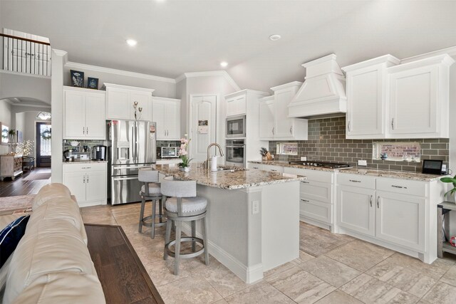 kitchen featuring stainless steel appliances, custom exhaust hood, white cabinetry, and tasteful backsplash