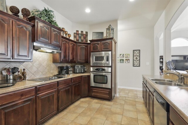 kitchen with arched walkways, under cabinet range hood, a sink, backsplash, and stainless steel appliances