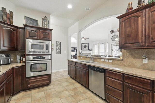 kitchen featuring ceiling fan, appliances with stainless steel finishes, a sink, arched walkways, and decorative backsplash