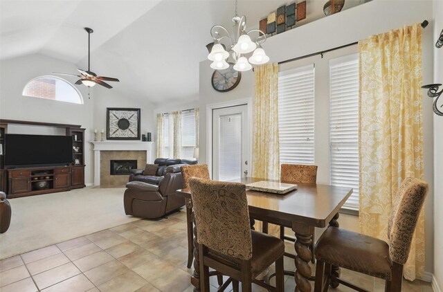 dining area featuring light carpet, a fireplace, high vaulted ceiling, ceiling fan with notable chandelier, and light tile patterned floors
