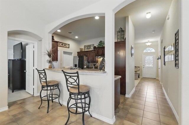 kitchen with stainless steel fridge, arched walkways, a breakfast bar area, and dark brown cabinetry