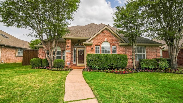 view of front of property featuring roof with shingles, a front yard, and brick siding