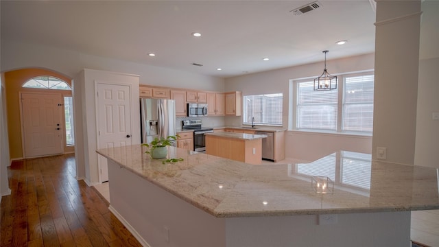 kitchen featuring visible vents, light brown cabinetry, appliances with stainless steel finishes, a center island, and a sink