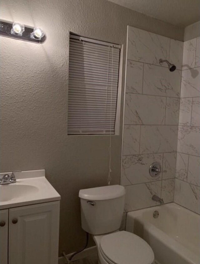 bathroom with toilet, a textured wall, bathing tub / shower combination, and vanity