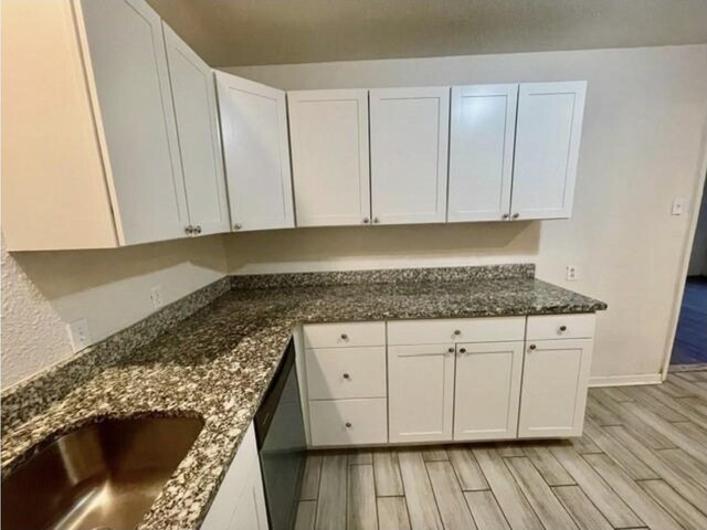 kitchen featuring a sink, light wood finished floors, dark stone countertops, and white cabinetry