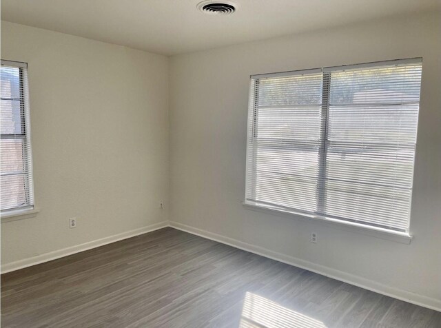empty room with baseboards, visible vents, and dark wood-type flooring