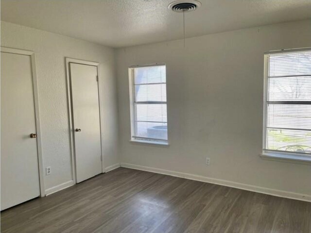 unfurnished bedroom with baseboards, multiple windows, and dark wood-style flooring