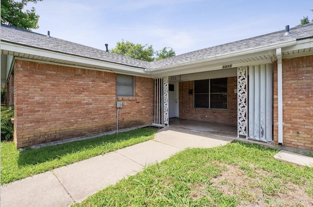 doorway to property with brick siding and roof with shingles