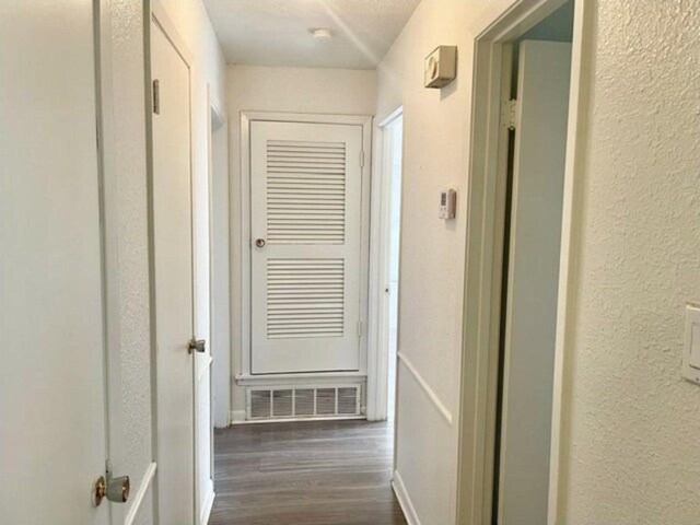 corridor with baseboards, visible vents, a textured wall, and dark wood-type flooring