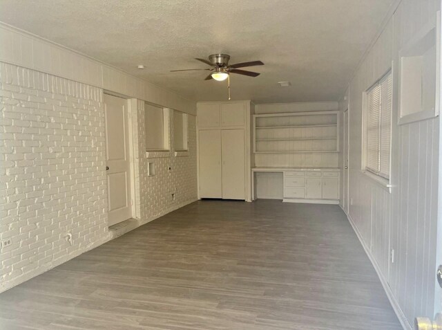 spare room featuring a textured ceiling, ceiling fan, wood finished floors, and brick wall