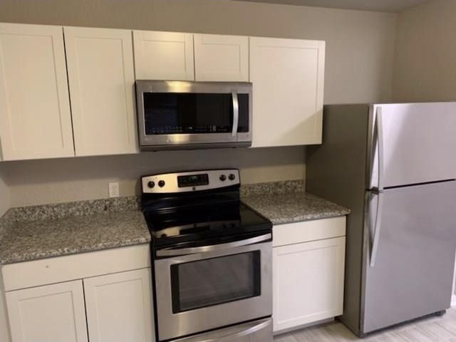 kitchen featuring white cabinets, appliances with stainless steel finishes, and light stone counters