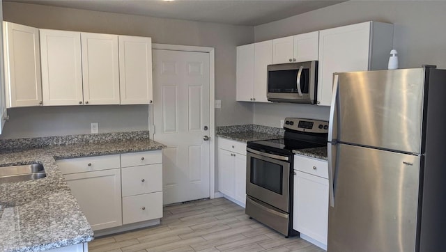 kitchen with white cabinetry, appliances with stainless steel finishes, a sink, and light wood-style floors