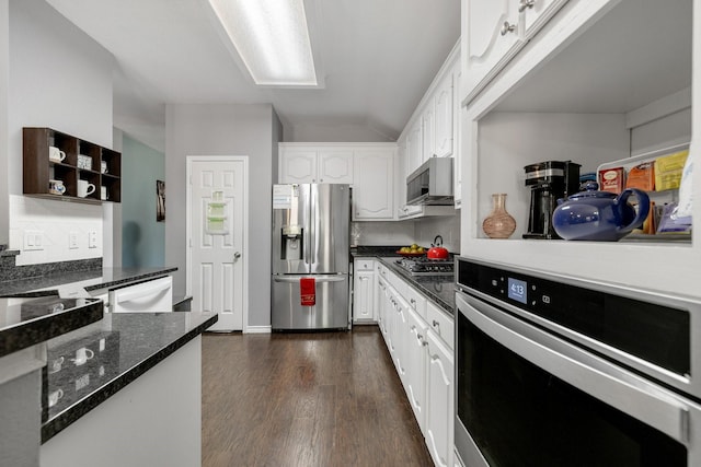 kitchen featuring white cabinets, dark stone countertops, stainless steel appliances, dark wood-type flooring, and vaulted ceiling