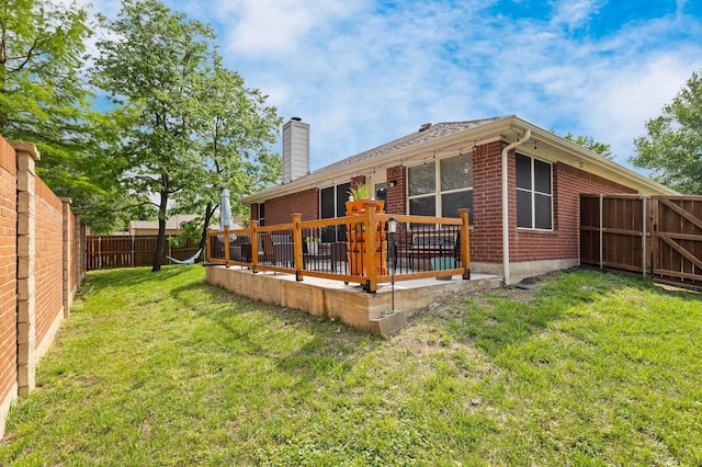 rear view of house with brick siding, a deck, a fenced backyard, a chimney, and a yard