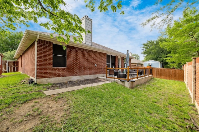 back of house with a fenced backyard, a chimney, a yard, and brick siding