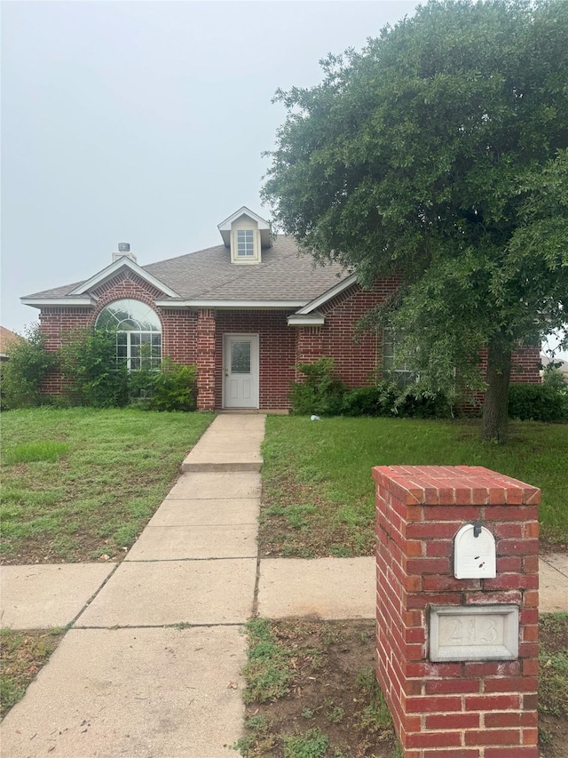 view of front of home with brick siding, a shingled roof, and a front lawn