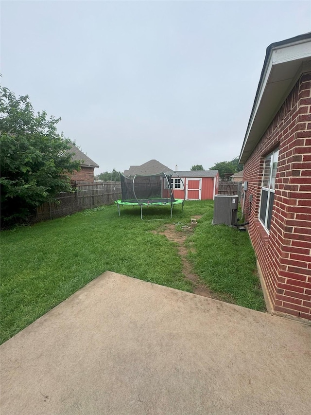 view of yard featuring fence, a trampoline, an outdoor structure, a storage shed, and a patio