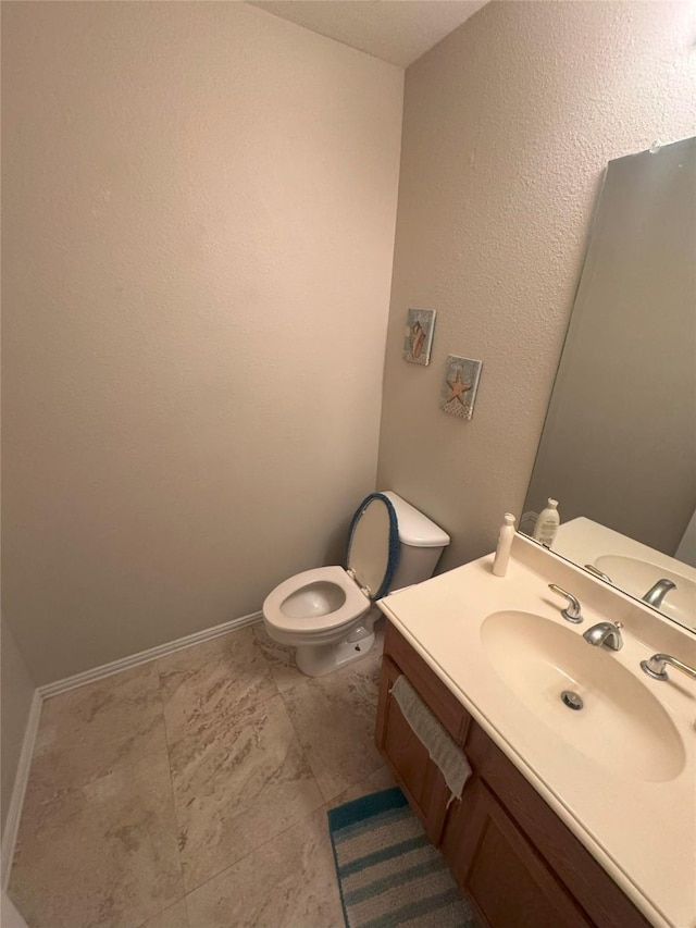 half bathroom featuring toilet, baseboards, and vanity