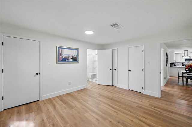 unfurnished bedroom featuring light wood finished floors, ensuite bath, two closets, baseboards, and visible vents