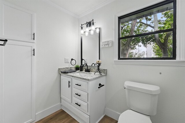 half bathroom with wood finished floors, baseboards, vanity, toilet, and ornamental molding