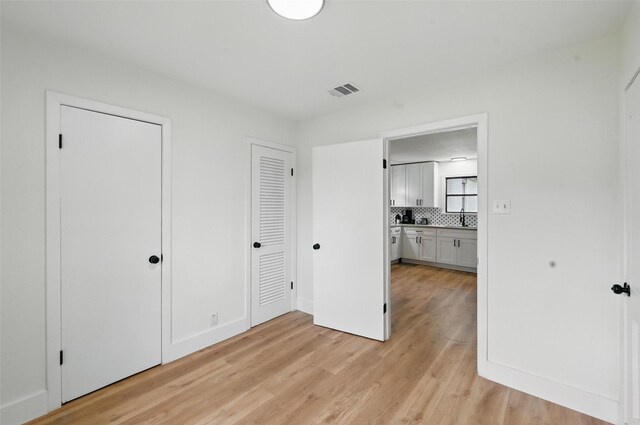 unfurnished bedroom with multiple closets, visible vents, a sink, and light wood-style floors
