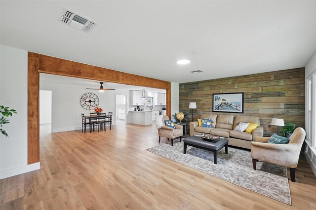 living room featuring wooden walls, baseboards, light wood-type flooring, and visible vents